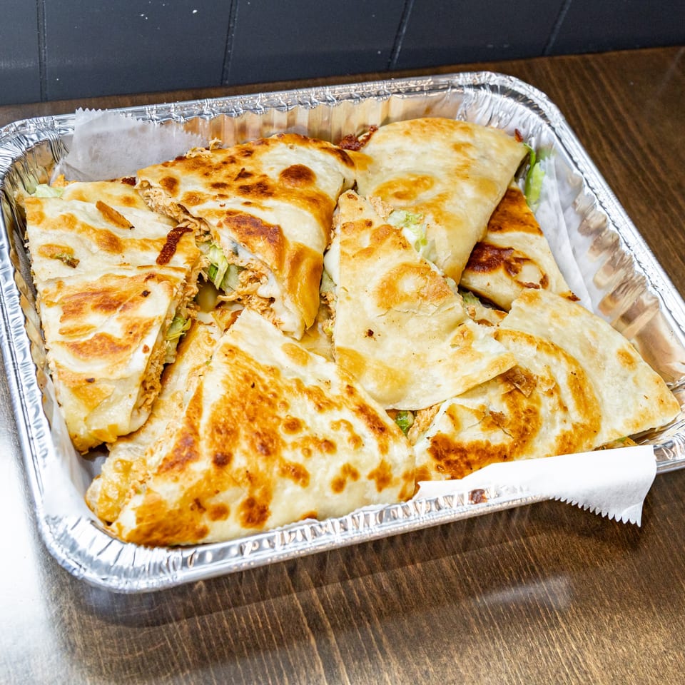 Guatemalan quesadillas, cut into triangles, with golden-brown tortillas and savory filling, in a foil container.