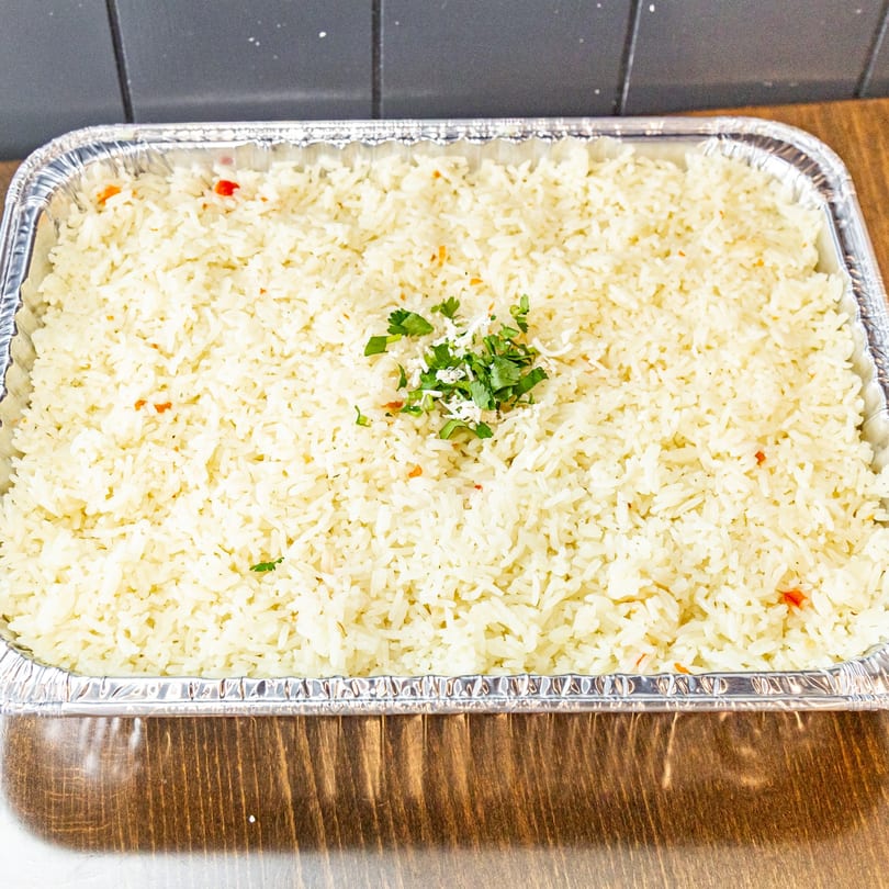 Large aluminum tray filled with white rice, garnished with fresh cilantro and shredded cheese.