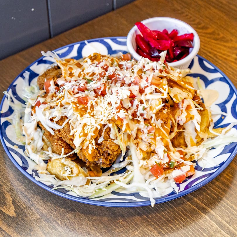 A Guatemalan tostada with fried chicken, cabbage, tomato, cheese, and sauce, with pickled vegetables.