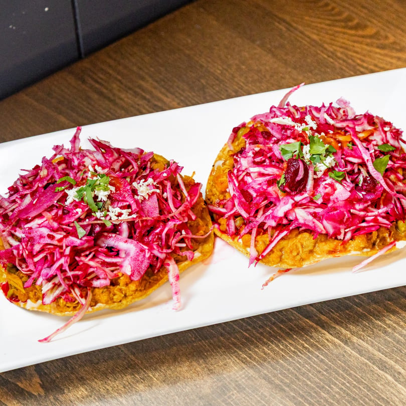 Two Guatemalan tostadas with refried beans, vibrant pink pickled cabbage, crumbled cheese, and cilantro.