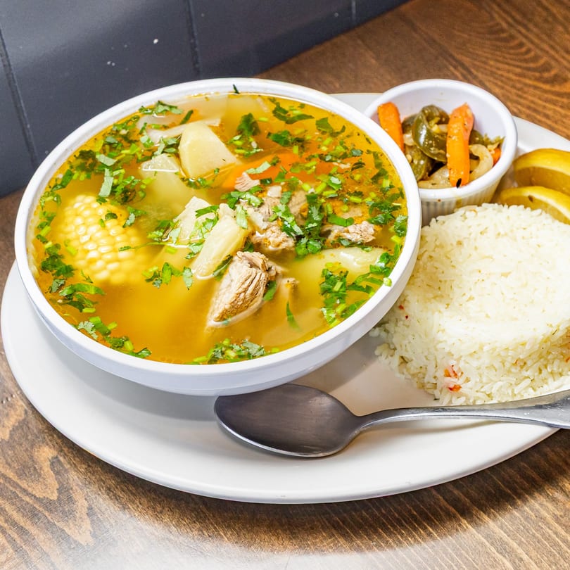 Guatemalan caldo de res, a beef soup with corn, potatoes, carrots, and cilantro, served with rice and pickled vegetables.