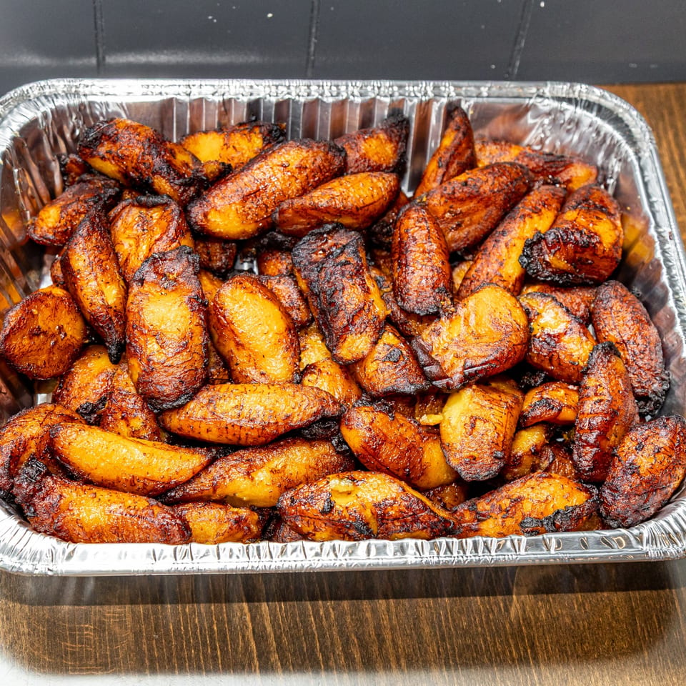 A foil tray filled with many golden-brown, caramelized Guatemalan fried plantains, some with dark, crispy edges.
